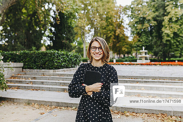 Smiling woman holding digital tablet in public park