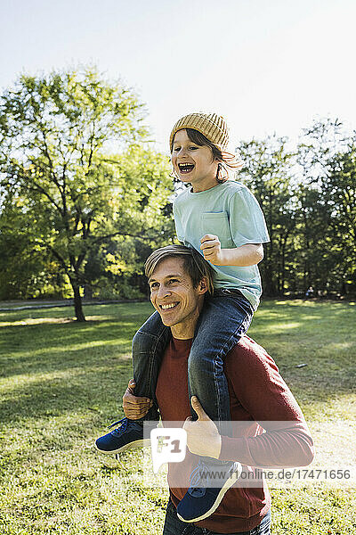 Father carrying cheerful son on shoulders in park