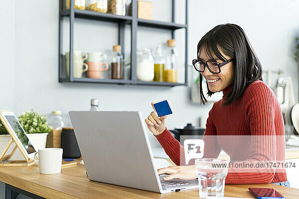 Businesswoman holding credit card working on laptop at home