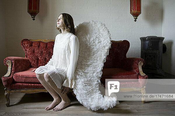 Teenage girl wearing angel costume contemplating at home