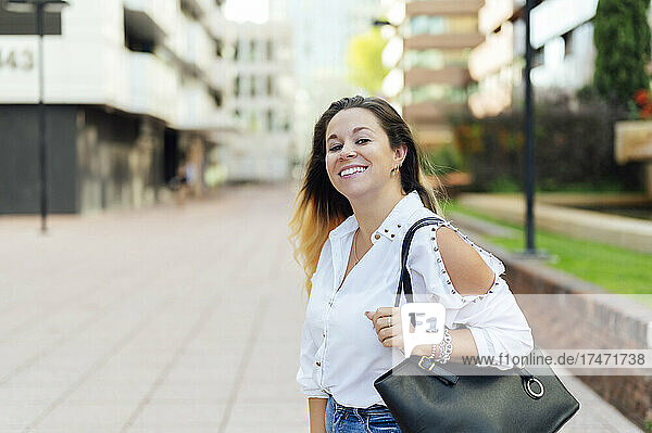 Smiling businesswoman with bag on footpath