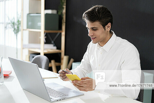 Young businessman using credit card through mobile phone while working in office