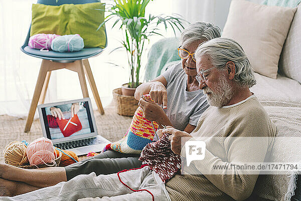 Senior woman teaching man to knit wool with needle at home