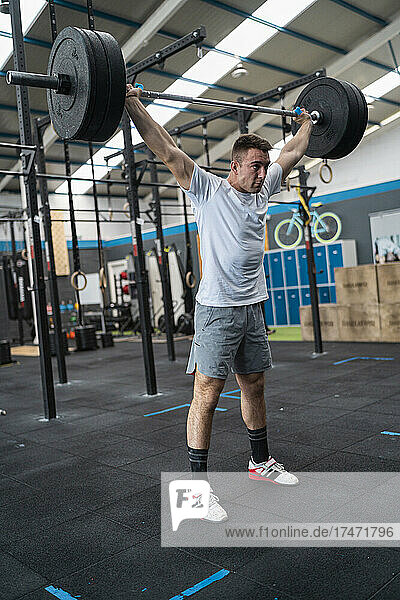 Confident sportsman holding barbell with weights in gym