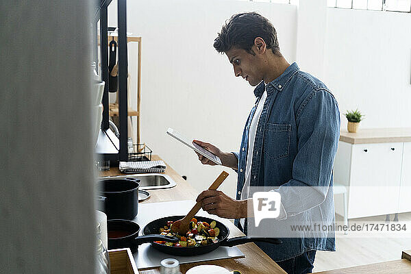 Mann nutzt digitales Tablet beim Zubereiten von Speisen in der Küche