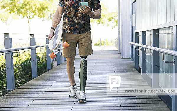 Man with prosthetic leg using mobile phone on boardwalk