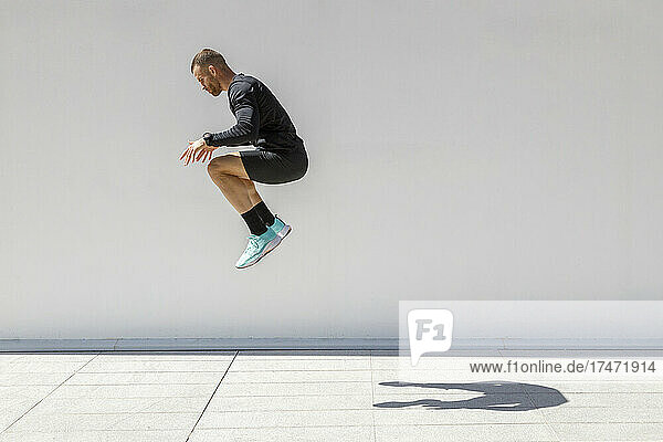 Male athlete jumping by wall during sunny day