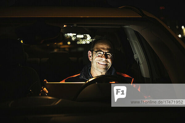Smiling engineer with laptop in car at night