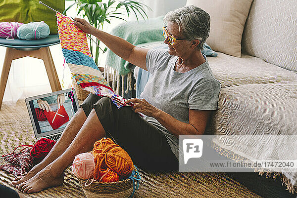 Woman with laptop checking knitted wool at home