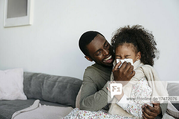 Happy father with tissue wiping daughter's nose at home