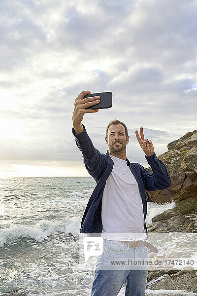 Man showing peace sign taking selfie at beach