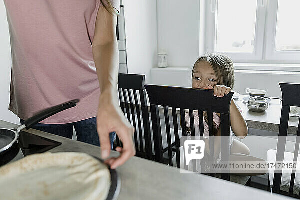 Girl looking at mother cooking pancake in kitchen