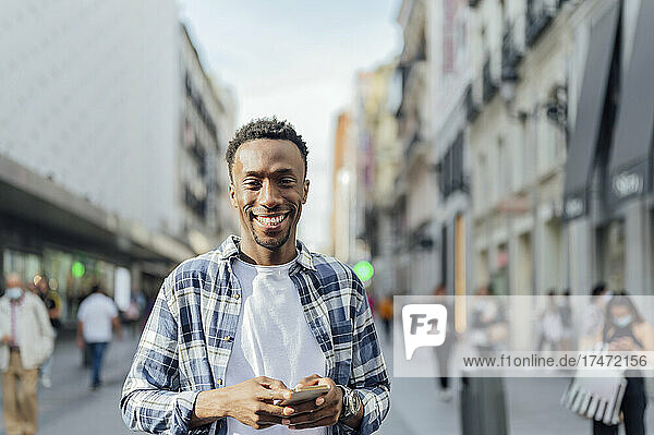Smiling man wearing plaid shirt holding smart phone in city