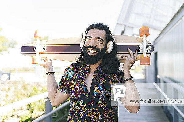 Happy man carrying skateboard on shoulder in park