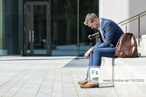 Sad businessman sitting with backpack on steps