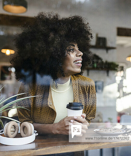 Lächelnde Frau mit Einwegkaffeetasse  die aus dem Fenster schaut