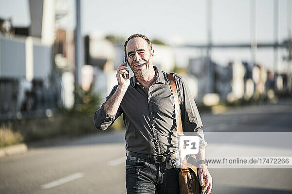 Cheerful businessman talking on smart phone while going for work
