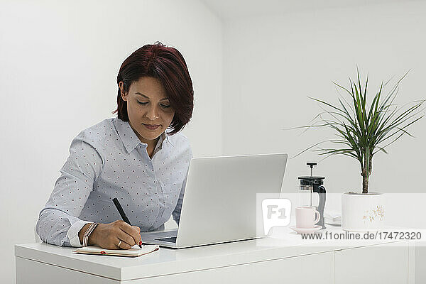Businesswoman writing in note pad while working at home office