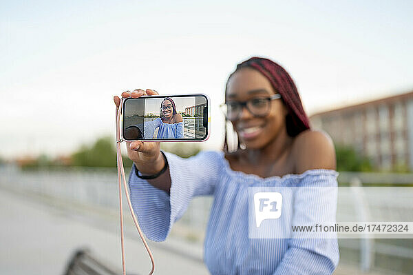 Smiling young woman taking selfie through mobile phone