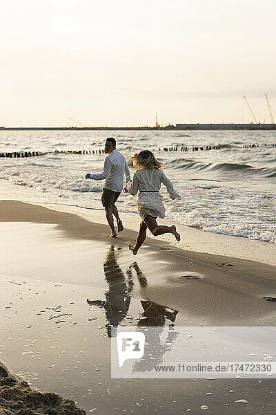 Young couple running at beach on sunset