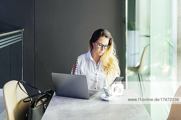 Female freelancer using smart phone in coffee shop