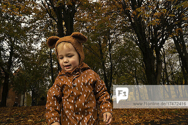 Toddler with brown cap and raincoat at autumn park