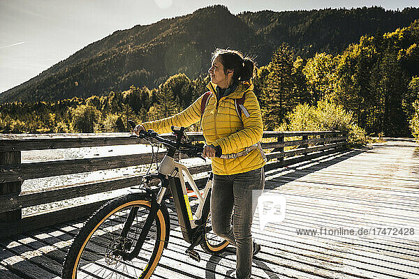 Smiling woman wheeling bicycle on bridge