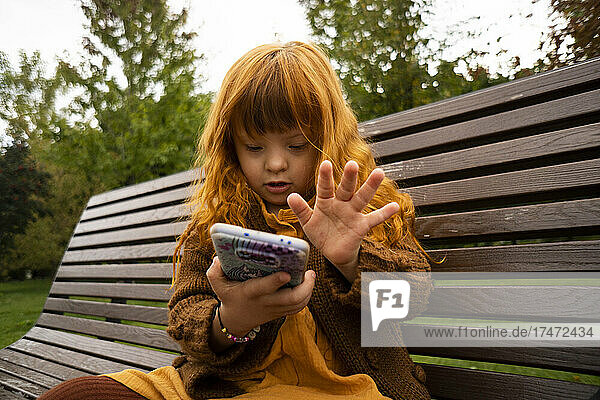 Redhead girl using mobile phone while sitting on park bench