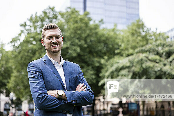 Smiling young businessman standing with arms crossed in city