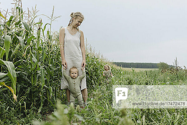 Woman assisting toddler girl to walk in corn field