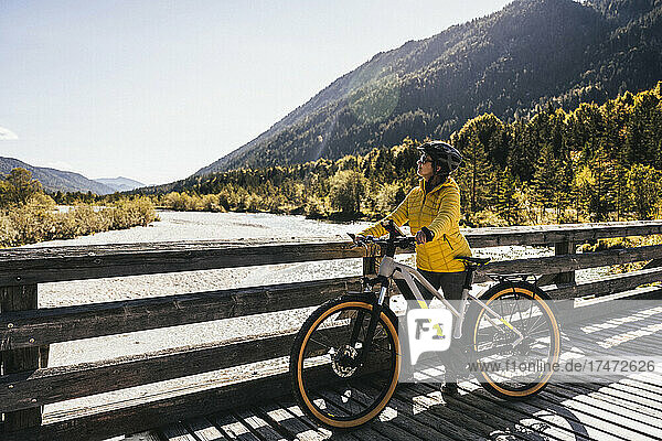 Woman with bicycle on bridge looking at mountains