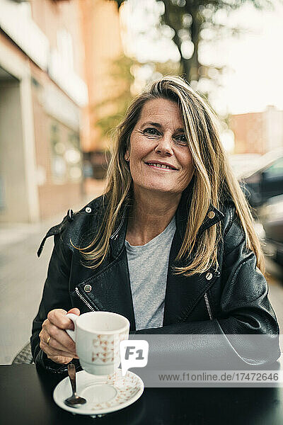Smiling mature woman holding cup while sitting at sidewalk cafe