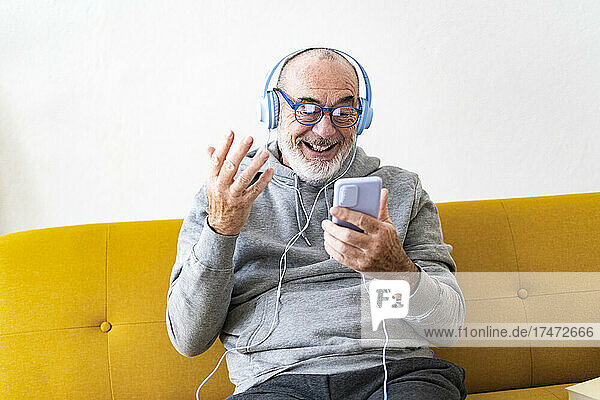 Man with headphones attending video call through mobile phone at home