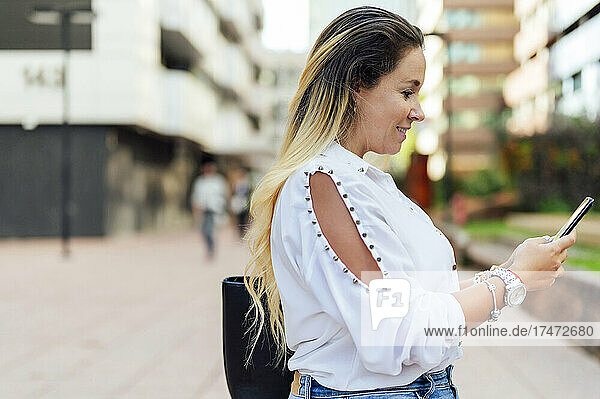 Smiling female freelancer using mobile phone on footpath