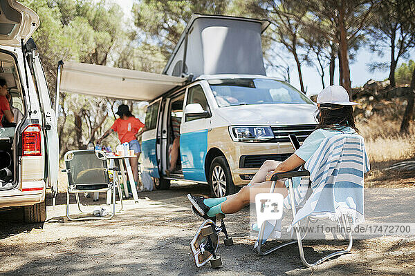 Woman with feet up sitting on chair by camper van