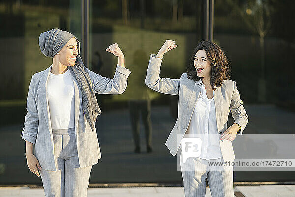 Happy female colleagues flexing muscles in front of glass wall