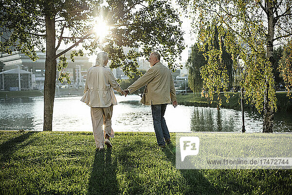 Couple holding hand while walking on grass by lake
