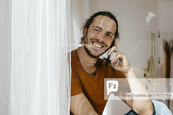 Smiling man talking on mobile phone while looking out of window