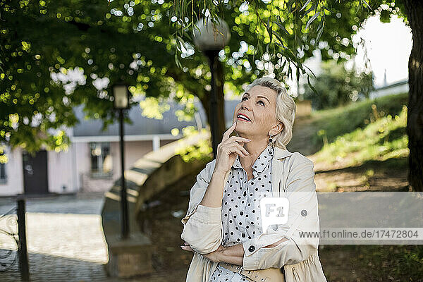 Thoughtful senior woman with hand on chin looking at branch