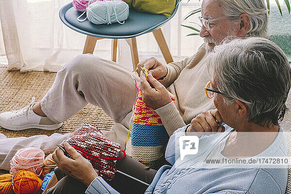 Woman looking at man knitting wool at home