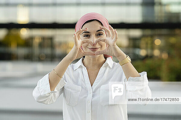 Smiling woman wearing hijab while gesturing heart shape
