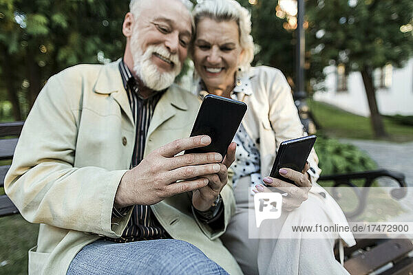 Paar benutzt Smartphone  während es auf Bank sitzt