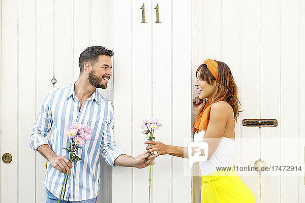 Man giving flowers to woman while leaning on white door