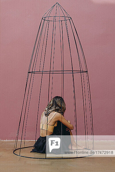 Woman with brown hair hugging knees while sitting in cage