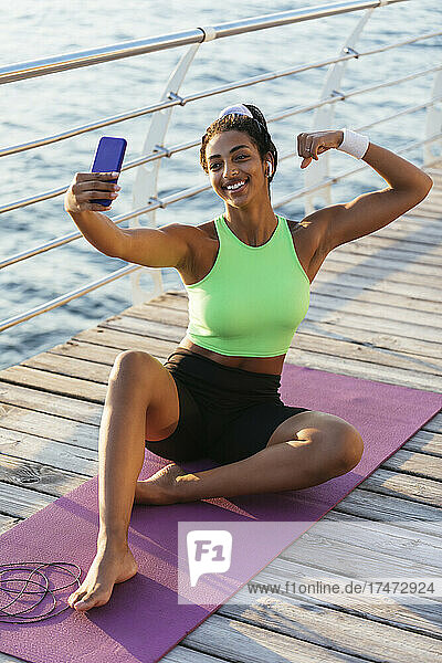 Glückliche Frau  die Muskeln spielen lässt  während sie mit dem Handy ein Selfie macht