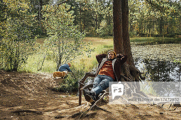 Man with hands behind head relaxing by tree in forest