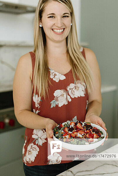 Smiling female professional holding garnished food plate in kitchen