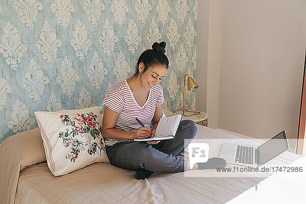 Smiling woman writing on diary in bedroom