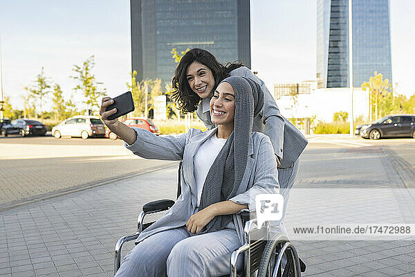Smiling disabled businesswoman taking selfie with female colleague on footpath