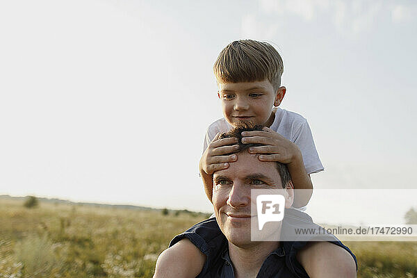 Smiling father carrying son on shoulders at meadow